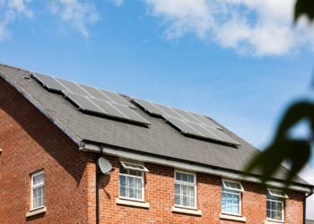Brick house with a row of solar panels on its roof under a clear blue sky