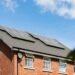 Brick house with a row of solar panels on its roof under a clear blue sky