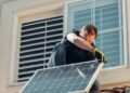 Man working on a house roof while installing a solar panel