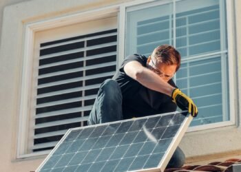 Man working on a house roof while installing a solar panel
