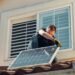 Man working on a house roof while installing a solar panel