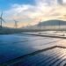 Solar panels and wind turbines silhouetted against the sky at sunset