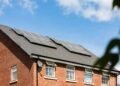 Solar panels mounted on the roof of an older brick house under a clear blue sky