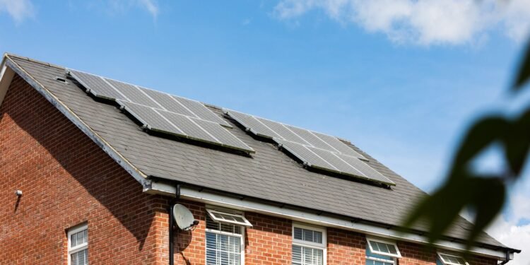 Solar panels mounted on the roof of an older brick house under a clear blue sky