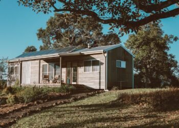 Wooden off-grid house with solar panels on its roof surrounded by green trees