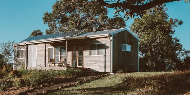 Wooden off-grid house with solar panels on its roof surrounded by green trees