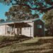 Wooden off-grid house with solar panels on its roof surrounded by green trees