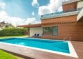 Backyard swimming pool with clear blue water beside a home under blue sky