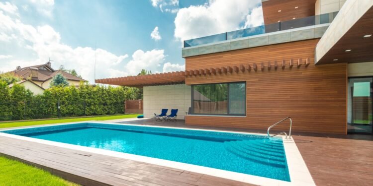 Backyard swimming pool with clear blue water beside a home under blue sky