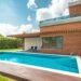 Backyard swimming pool with clear blue water beside a home under blue sky