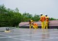 Two men cleaning dust off a row of solar panels with brushes and water