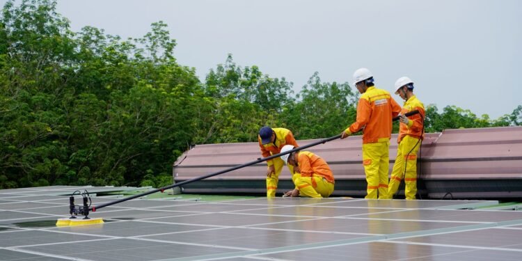 Two men cleaning dust off a row of solar panels with brushes and water