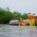 Two men cleaning dust off a row of solar panels with brushes and water