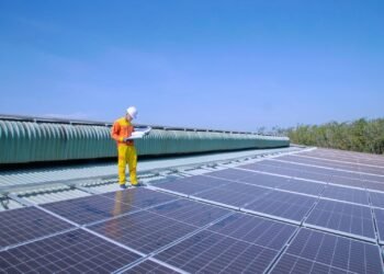 Solar technician working on rows of solar panels on a rooftop under a clear sky