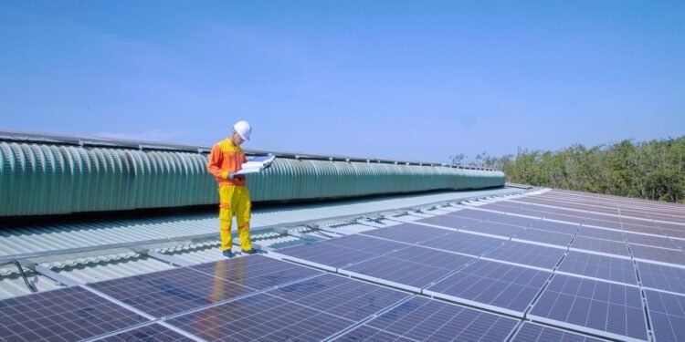 Solar technician working on rows of solar panels on a rooftop under a clear sky