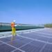 Solar technician working on rows of solar panels on a rooftop under a clear sky