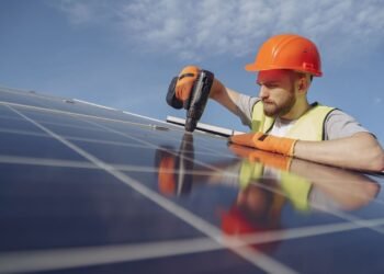 Electrician in work gear installing and wiring a solar panel on a mounting frame
