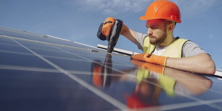 Electrician in work gear installing and wiring a solar panel on a mounting frame