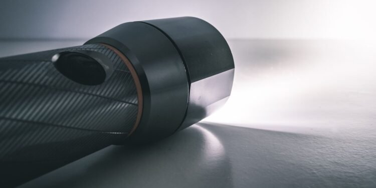 Black handheld flashlight switched on, shining a bright beam of white light