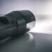 Black handheld flashlight switched on, shining a bright beam of white light