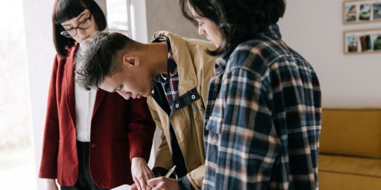 Man signing loan documents beside a woman while an agent looks on