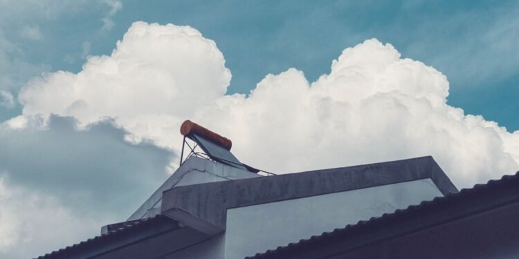 Solar water heater tank with evacuated glass tubes mounted on a building rooftop under a cloudy sky