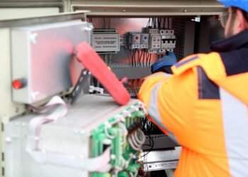 Technician checking and maintaining a wall-mounted solar inverter and its wiring